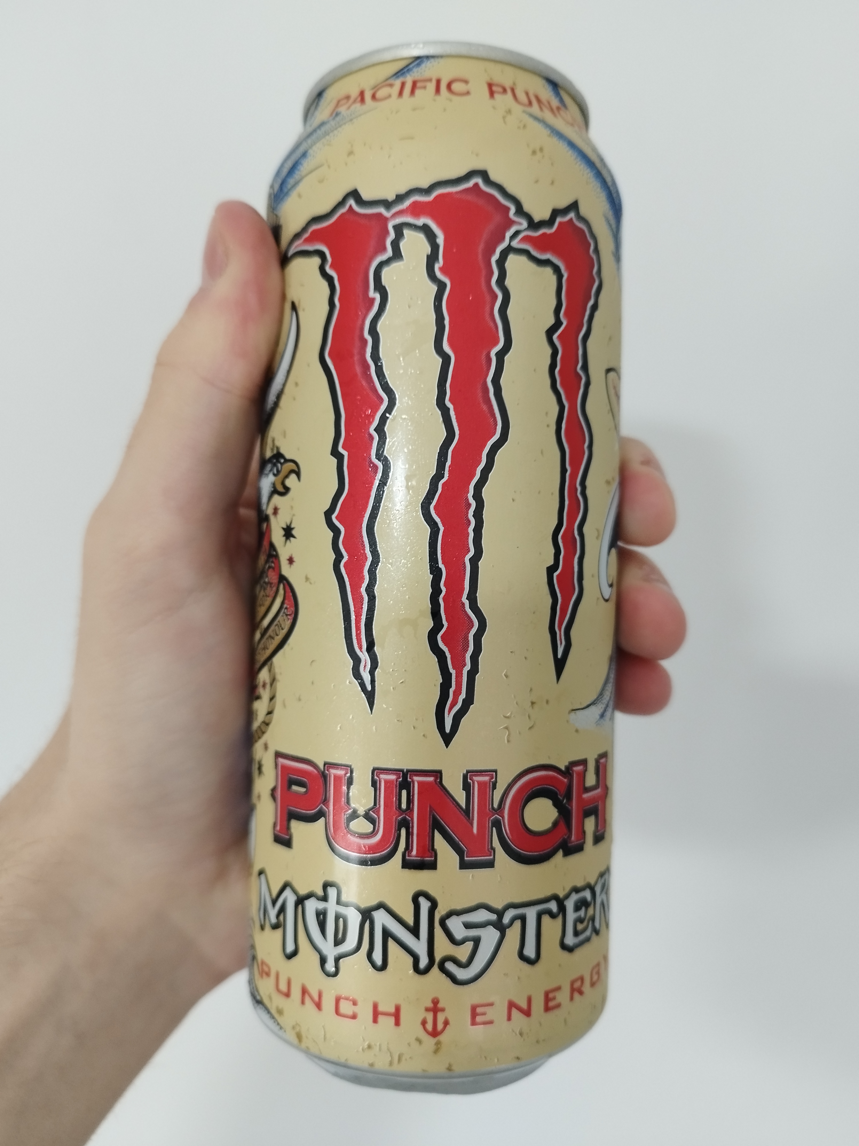 a beige-ish yellow-ish can of punch monster pacific punch. the monster logo and the word 'punch' are in red. there are illustrations of a sailing ship, eagles, a shark, a compass.